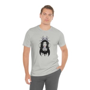 Può includere: Una t-shirt color grigio melange con una grafica in bianco e nero di una donna con lunghi capelli neri che indossa una collana e una corona di spine. La donna è circondata da una luna crescente e stelle.