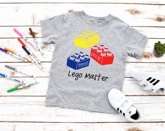 May include: A gray t-shirt with a design of three colorful Lego bricks and the text "Lego Master" printed on the front.