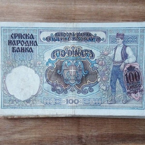 May include: A vintage 100 dinar banknote from the Serbian National Bank. The note features a blue and brown design with a coat of arms and a portrait of a man in traditional clothing.