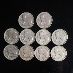 Pode incluir: Dez moedas irlandesas de prata com um desenho de lebre. Cada moeda tem o texto "Leag" e "Reut", juntamente com o número "3d".