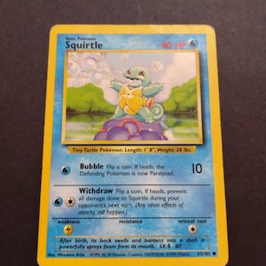 May include: A blue and yellow Squirtle Pokemon card from the 1999 Wizards of the Coast set. The card features an illustration of Squirtle blowing bubbles. The card text reads "Bubble: Flip a coin. If heads, the Defending Pokemon is now Paralyzed." and "Withdraw: Flip a coin. If heads, prevent all damage done to Squirtle during your opponent's next turn. (Any other effects of attacks still happen.)"