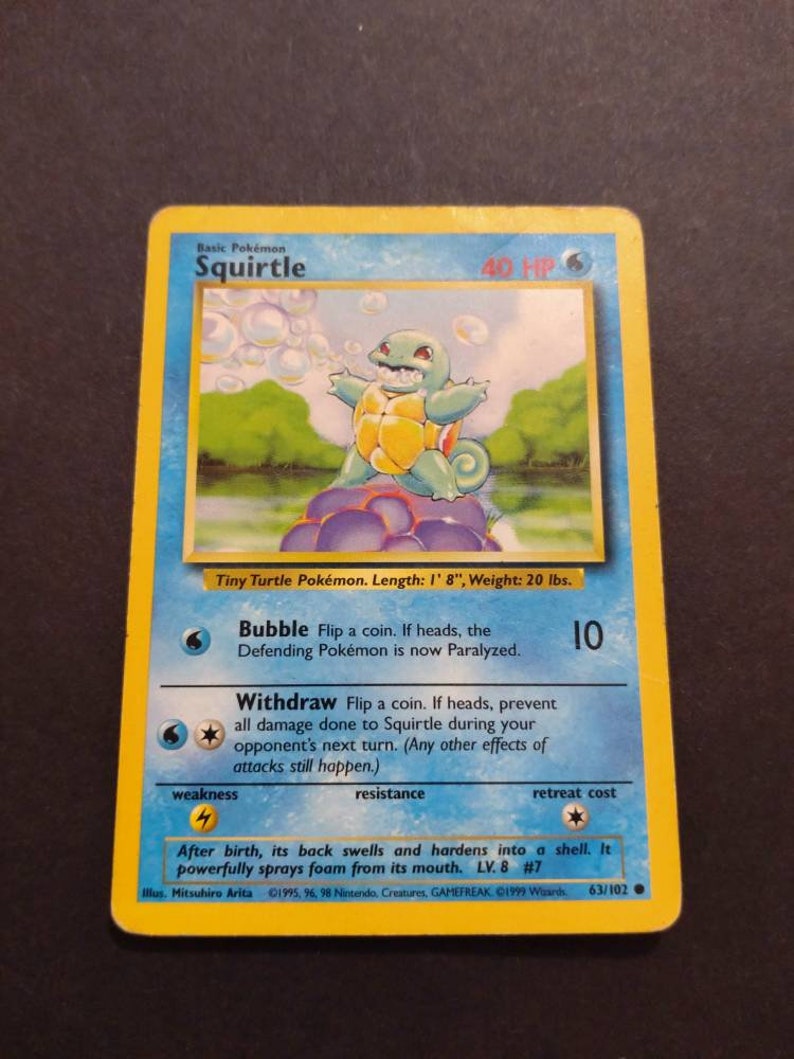 May include: A blue and yellow Squirtle Pokemon card from the 1999 Wizards of the Coast set. The card features an illustration of Squirtle blowing bubbles. The card text reads "Bubble: Flip a coin. If heads, the Defending Pokemon is now Paralyzed." and "Withdraw: Flip a coin. If heads, prevent all damage done to Squirtle during your opponent's next turn. (Any other effects of attacks still happen.)"