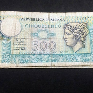 Può includere: Una vecchia banconota italiana da 500 lire con la scritta REPUBBLICA ITALIANA e CINQUECENTO. La banconota mostra il ritratto di profilo di una figura alata sulla destra, il numero 500 al centro e complessi motivi geometrici color verde acqua e giallo.