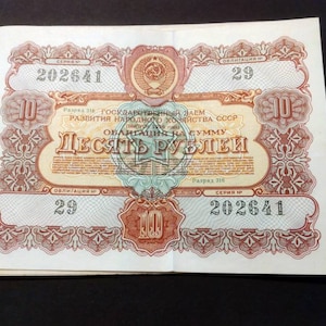 May include: A vintage Soviet bond with a red and white design. The bond is for ten rubles and has the text "Государственный заем развития народного хозяйства СССР" (State Loan for the Development of the National Economy of the USSR) printed on it.