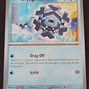 May include: A Cryogonal trading card with 90 HP, featuring a blue and grey geometric ice creature. The card displays the attacks Drag Off and Icicle, with text detailing the Pokémon's height of 3'7" and weight of 326.3 lbs, dated 2025 Pokémon.