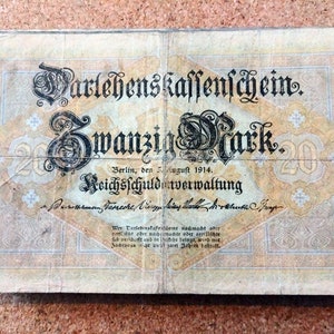 May include: A vintage German 20 Mark Darlehens Kassenschein (loan bond) from August 1914. The bond is printed on paper with a light yellow background and features black text and ornate designs. The text reads "Darlehens Kassenschein" (loan bond), "Zwanzig Mark" (twenty marks), "Berlin, den 5 August 1914" (Berlin, August 5, 1914), and "Reichsschuldverwaltung" (Reich Debt Administration).