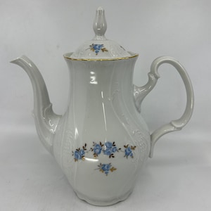 May include: White porcelain coffee pot with a gold trim and blue floral design. The pot has a lid with a knob on top.