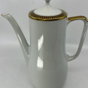 May include: White ceramic coffee pot with a gold trim and lid. The pot has a spout and a handle.