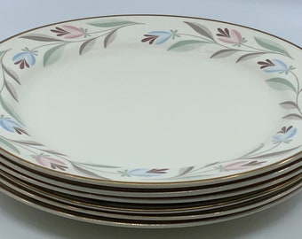 May include: A stack of six white ceramic dinner plates with a gold rim and a floral design in shades of pink, blue, and green.