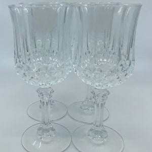 May include: Set of four clear glass wine glasses with a cut crystal design. The glasses have a tall, slender stem and a wide bowl.