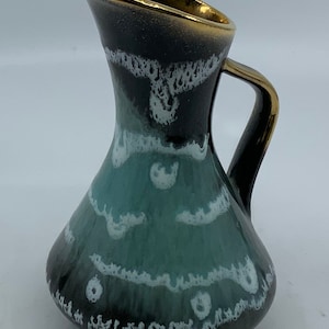May include: A small, green and black ceramic pitcher with a white and gold design. The pitcher has a rounded body and a small handle.