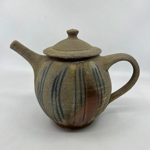 May include: A brown ceramic teapot with a lid and a handle. The teapot has a striped pattern in shades of brown, blue, and red.