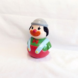 May include: A red, green and blue plastic toy clown with a grey hat and a red bow tie. The clown is a roly-poly toy that can be tipped over and will right itself.