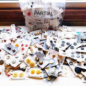May include: A large collection of assorted buttons in various colours, shapes, and sizes. The buttons are packaged in plastic bags and on cards. The text "PARTIAL" is visible on one of the bags.