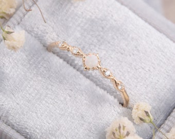 May include: A delicate gold ring featuring a white opal gemstone and small diamonds set in a delicate floral design. The ring is displayed in a grey velvet ring box.