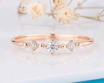 May include: A rose gold ring featuring a central round brilliant-cut diamond flanked by two smaller round diamonds, all set in a delicate band with small metal bead accents between each stone, creating a refined and symmetrical jewellery piece.