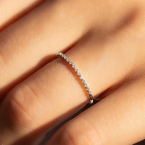 Puede incluir: Un delicado anillo de banda de plata con una fila de pequeñas piedras preciosas transparentes.