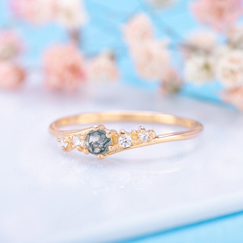 Pode incluir: Um delicado anel de ouro com uma gema de &aacute;gata verde musgo e pequenos diamantes transparentes. O anel tem uma banda curva e um grupo de diamantes de um lado.