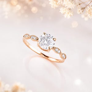May include: A rose gold ring featuring a large, round, brilliant-cut center stone held by four prongs. The band is accented with small, marquise-shaped settings, each containing a tiny round diamond, extending along the sides of the center stone.