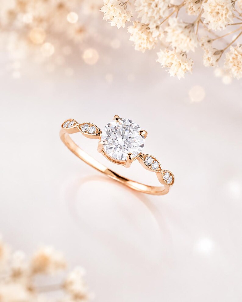 May include: A rose gold ring featuring a large, round, brilliant-cut center stone held by four prongs. The band is accented with small, marquise-shaped settings, each containing a tiny round diamond, extending along the sides of the center stone.