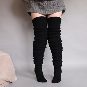 May include: A pair of black thigh-high socks made of knitted fabric. The socks are folded down at the top and have a ribbed texture.