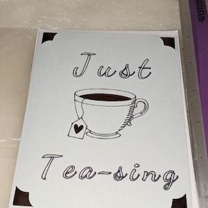 May include: A light blue card with black text that reads "Just Tea-sing" and a black and white illustration of a teacup with a tea bag.