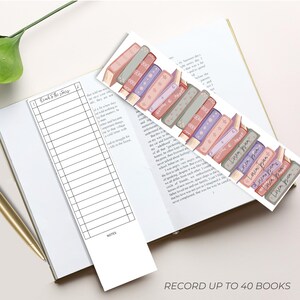 K&ouml;nnte beinhalten: Ein offenes Buch mit zwei Lesezeichen und einem goldenen Stift. Ein Lesezeichen ist eine Leseliste, das andere zeigt einen Stapel bunter B&uuml;cher. Der Text "Record up to 40 books" ist sichtbar.