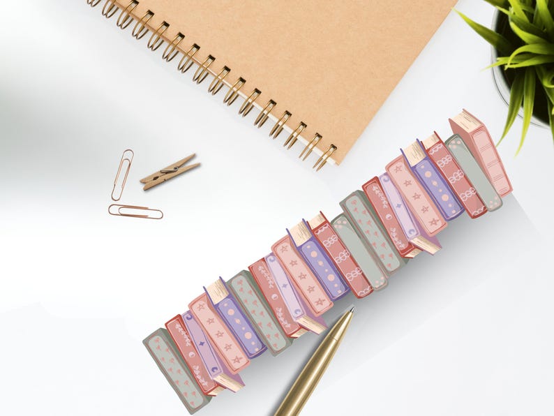 K&ouml;nnte beinhalten: Eine Sammlung dekorativer B&uuml;roklammern in Buchform in verschiedenen Farben, darunter Rosa, Lila und Grau, diagonal auf einer wei&szlig;en Oberfl&auml;che angeordnet. Ein goldener Stift, ein Spiralnotizbuch und andere B&uuml;roartikel sind ebenfalls vorhanden.