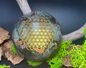 Può includere: Una sfera verde e dorata con un designo a fiore della vita. La sfera è realizzata in pietra naturale e ha una finitura dorata metallica.