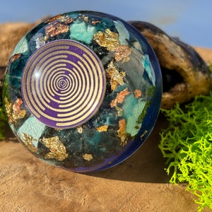 Könnte beinhalten: Eine runde, klare Harz-Kugel mit einem eingebetteten Spiraldesign in Lila und Gold. Die Kugel ist mit blauen, grünen und goldenen Flocken gefüllt.