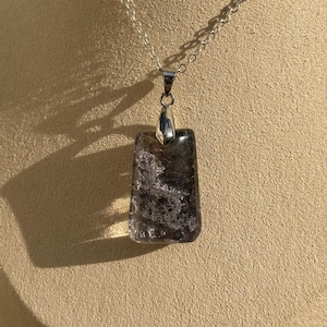 May include: A silver chain necklace with a rectangular pendant made of clear quartz with black and grey inclusions.