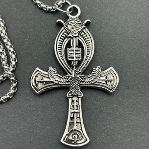 Peut inclure: Un collier avec un pendentif Ankh en argent, avec un design détaillé représentant un scarabée ailé égyptien et l'œil d'Horus. Le collier est doté d'une chaîne en argent.