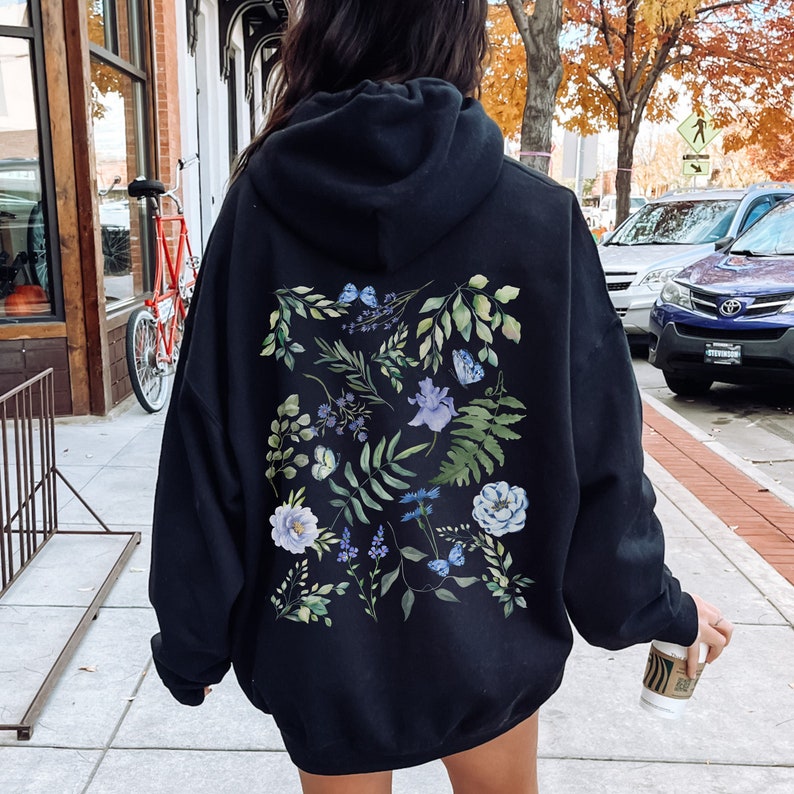 May include: Black oversized hoodie with a floral print on the back. The print features blue and green flowers, leaves, and butterflies.