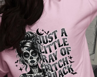 May include: Pink sweatshirt with a black and white graphic of a woman with a sugar skull face. The text "Just a little ray of pitch black" is printed on the sweatshirt.