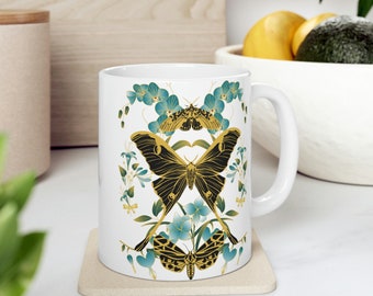May include: White ceramic mug with a black and gold butterfly design. The butterfly is surrounded by blue and green flowers. The mug has a handle on the right side.