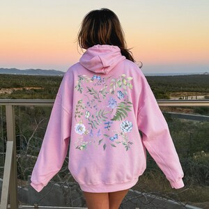 May include: A pink hoodie with a floral print on the back. The print features blue flowers, green leaves, and butterflies.