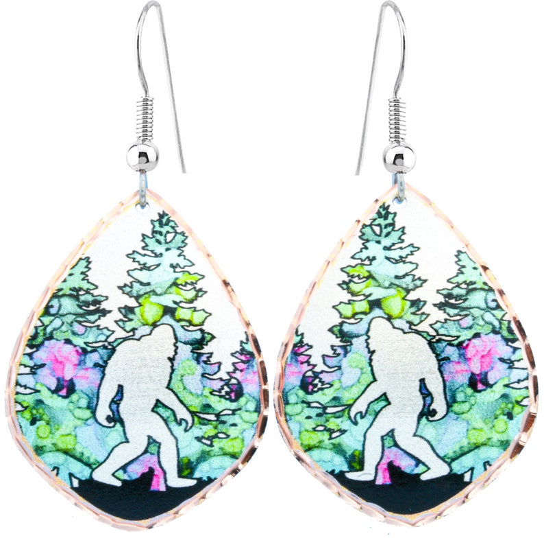 May include: A pair of silver dangle earrings with a teardrop-shaped design. Each earring features a watercolor-style image of a white silhouette of Bigfoot walking through a forest with green and pink trees.