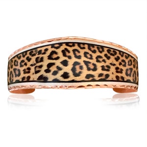 May include: A copper cuff bracelet with a white and black leopard print design. The bracelet has a hammered texture and a white border.