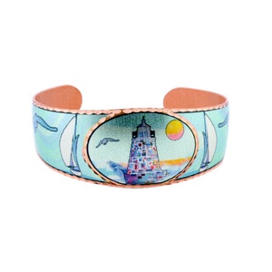 May include: A copper bracelet with a blue and white enamel design featuring a lighthouse, sailboat, and seagulls. The bracelet has a hammered copper finish.