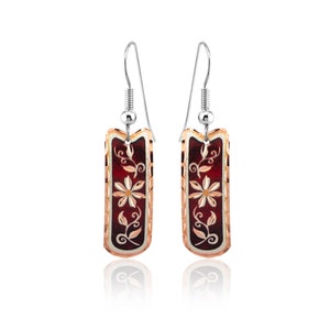 May include: A pair of silver dangle earrings with a red and gold rectangular pendant featuring a floral design.