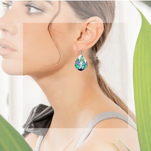 May include: A pair of silver dangle earrings with a teardrop-shaped design. The earrings feature a colorful image of a Bigfoot walking through a forest.