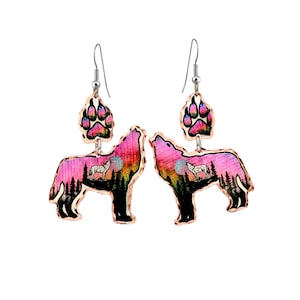 May include: A pair of copper-colored earrings featuring a howling wolf design. The earrings have a paw print at the top and a wolf silhouette against a pink and orange sunset. The earrings are suspended from silver-colored hooks.