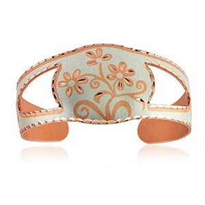 May include: A wide cuff bracelet featuring a two-tone design with a metallic copper base and a matte light green centre panel. The centre panel is decorated with an engraved floral pattern in copper, and the edges have a textured, scalloped border.