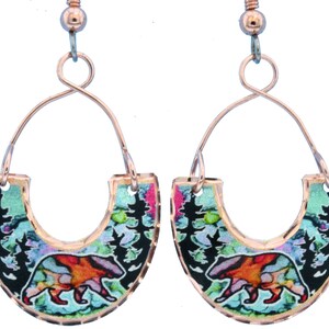 May include: A pair of copper hoop earrings with a colorful bear and forest scene design. The earrings are made of copper wire and have a unique, handmade look.