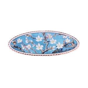 May include: An oval-shaped, blue and white ceramic tile with a gold trim. The tile features a painting of a blooming almond tree branch with white flowers against a blue sky. The text "Vincent van Gogh" is visible in the lower right corner of the tile.