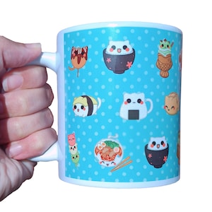 May include: A white ceramic mug featuring a bright blue background with a white polka dot pattern. The surface is decorated with various cute cartoon cats integrated into Japanese food illustrations, including sushi, ramen, and taiyaki treats.