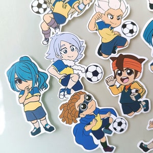 May include: A set of nine cartoon stickers featuring characters playing soccer. The characters are wearing yellow and blue uniforms and have different hairstyles and expressions. The stickers are printed on white paper and have a glossy finish.