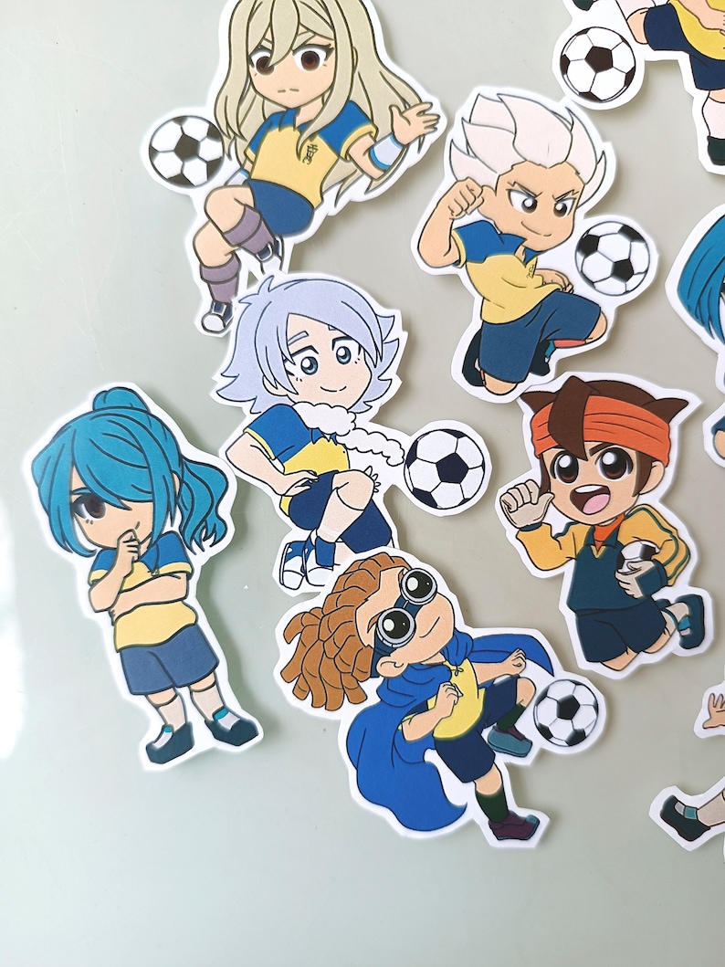 May include: A set of nine cartoon stickers featuring characters playing soccer. The characters are wearing yellow and blue uniforms and have different hairstyles and expressions. The stickers are printed on white paper and have a glossy finish.