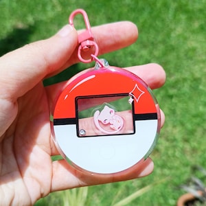 May include: A pink and white Pok&eacute; Ball keychain with a clear plastic design. A pink Pok&eacute;mon character is visible inside the Pok&eacute; Ball.