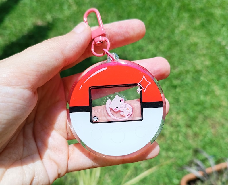 May include: A pink and white Pok&eacute; Ball keychain with a clear plastic design. A pink Pok&eacute;mon character is visible inside the Pok&eacute; Ball.